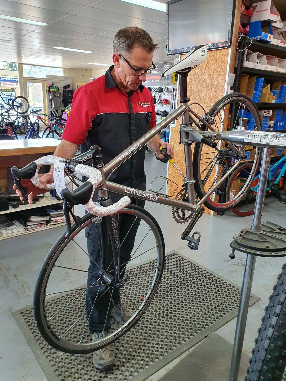 Man in red shirt working on a bicycle in a bike shop.