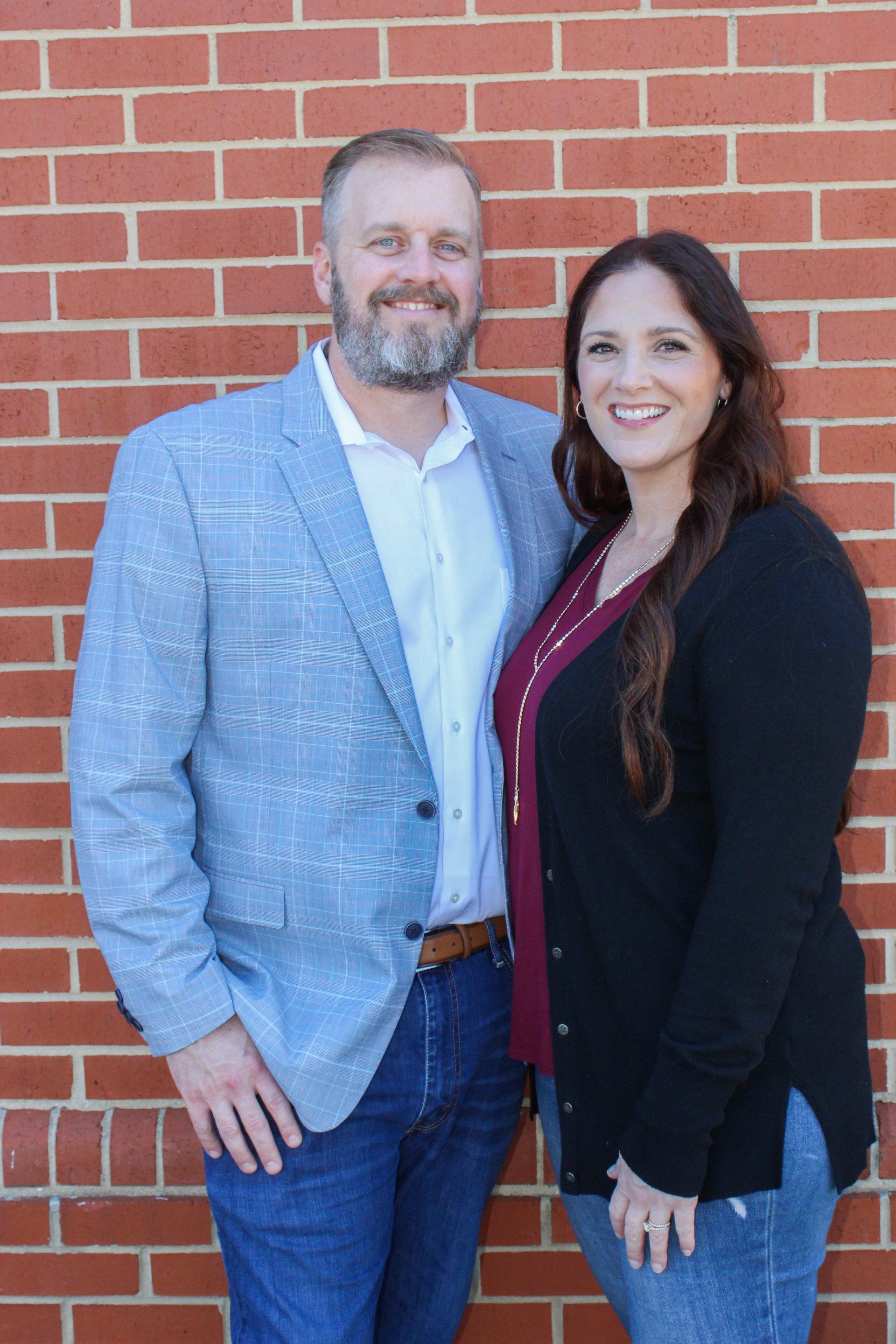 A man and a woman are posing for a picture in front of a brick wall.