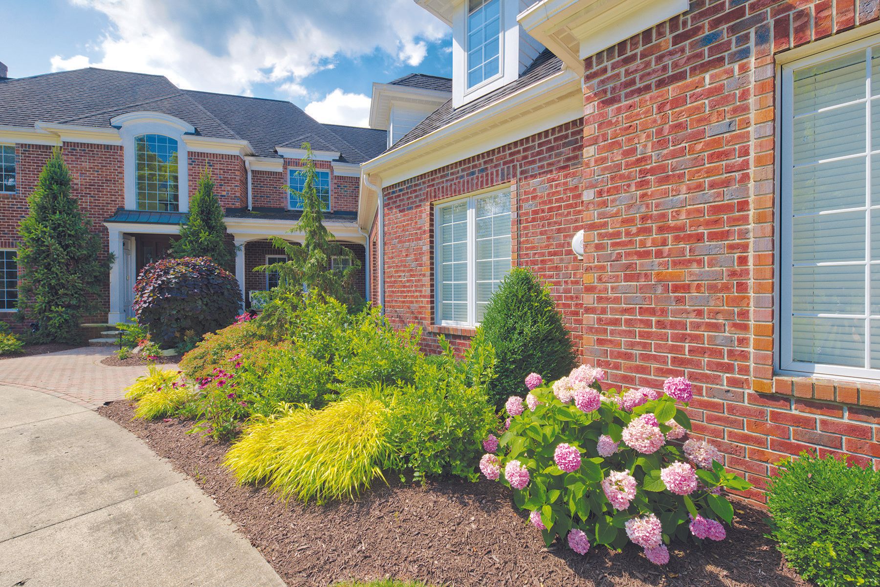 Brick house with landscaped garden, pathway, and vibrant flowers.