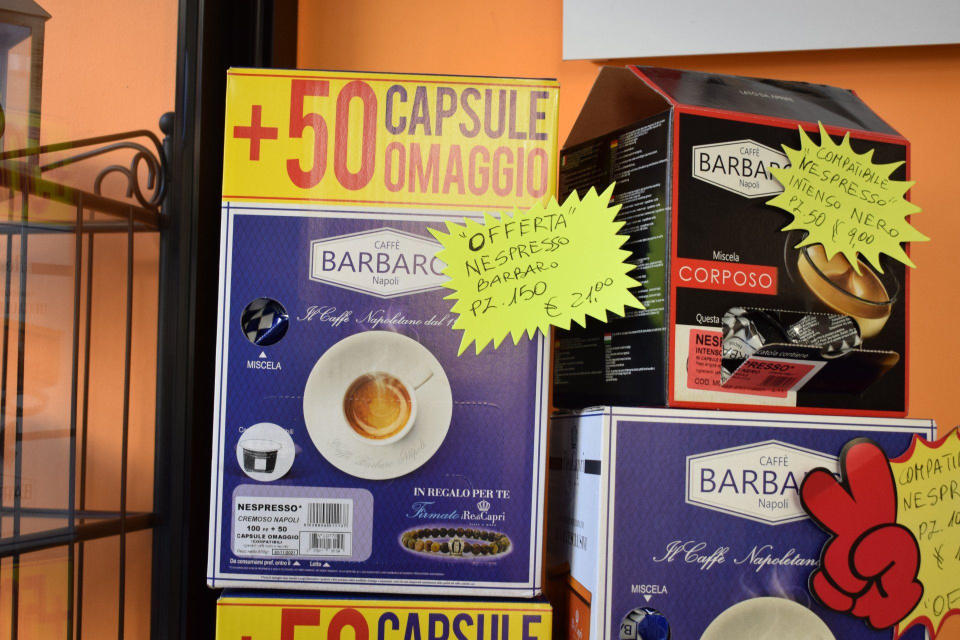 Capsule di caffè esposte in un negozio, con cartelli promozionali gialli e rossi.