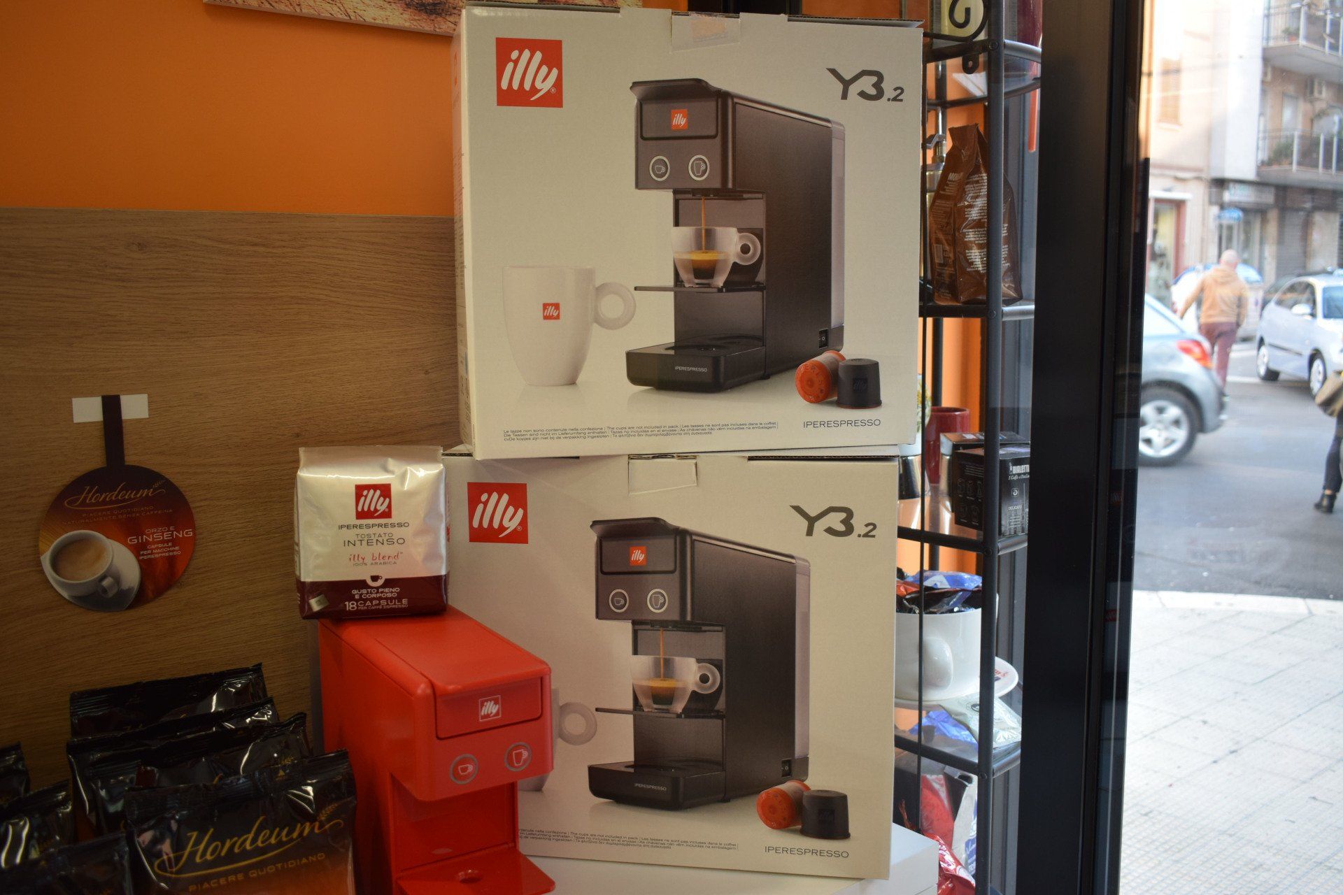 Scatole di macchine per caffè espresso Illy Y3.3 esposte in un negozio, con forniture per il caffè e vista sulla strada.