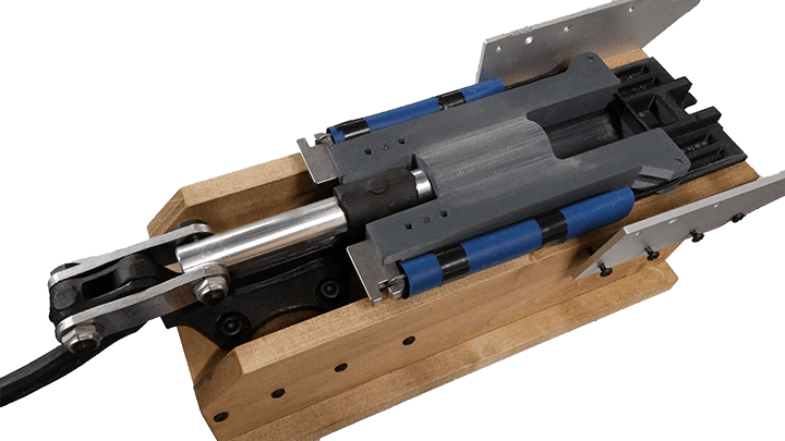 A machined piston device mounted on a wooden frame.