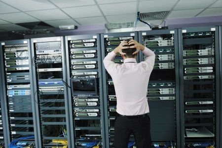 A man facing six server racks, with his hands on his head in exasperation