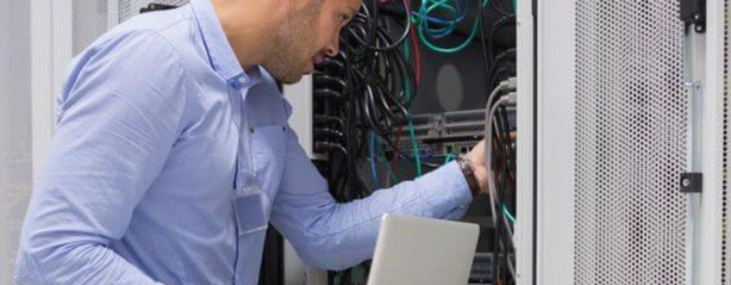 A man with a laptop moving wires in a server rack