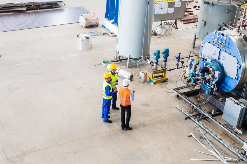 Three workers with hard hats and high visibility vests next to large industrial equipment
