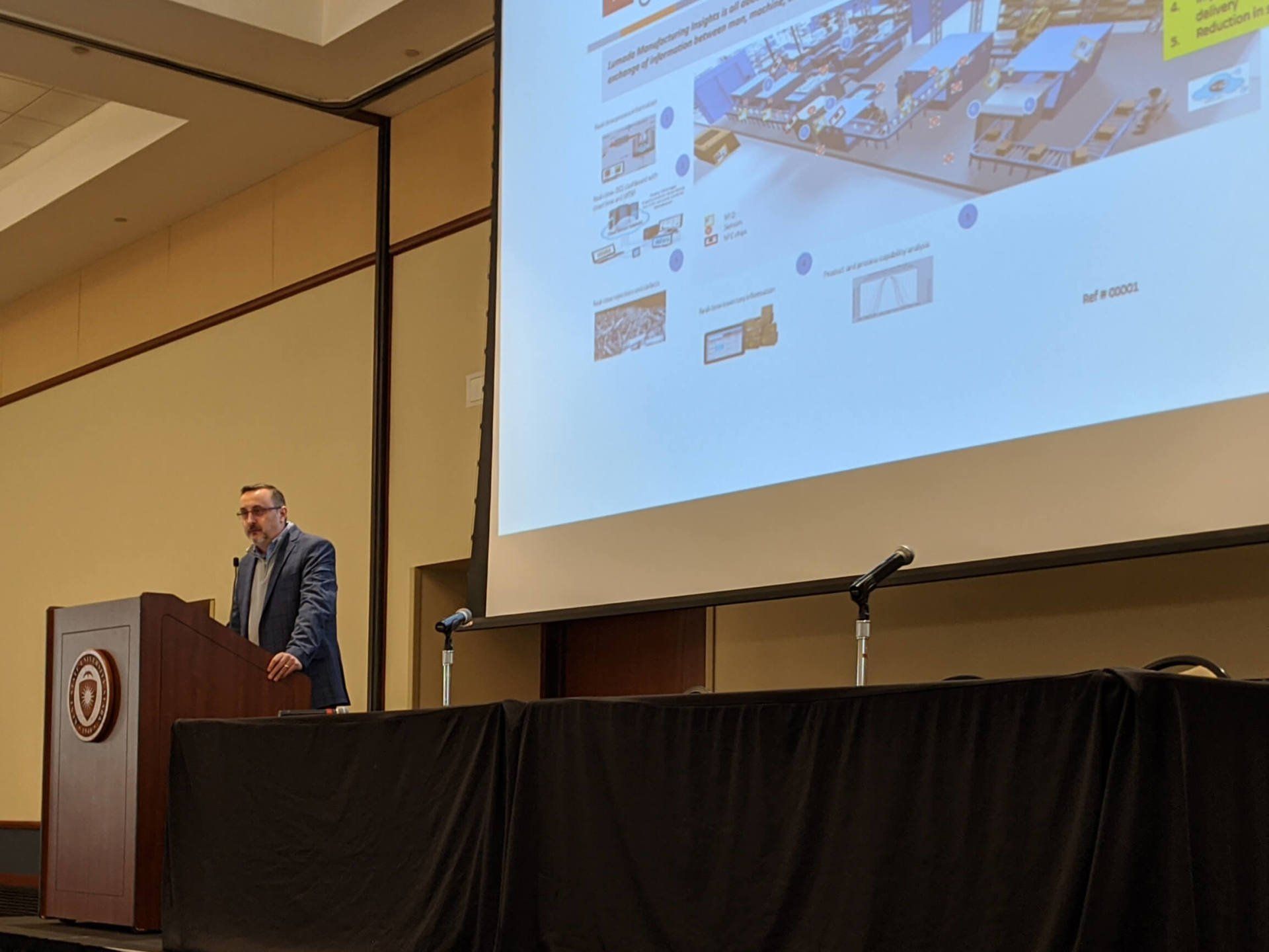 A man speaking into a microphone. A presentation slide is projected behind him
