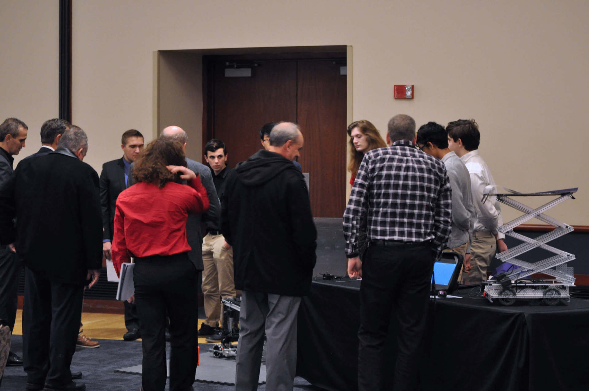 A couple of students are showcasing a robot, the view of which is obstructed by some people who are gathered around.