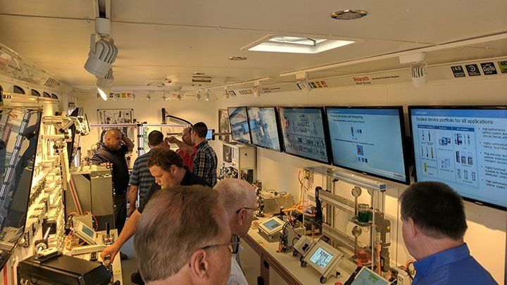 Nine people inside a trailer with various computers and equipment on display inside of it.