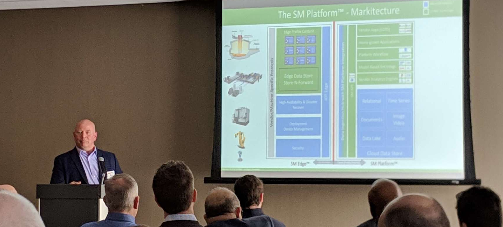 A man giving a presentation. On the slide is info about SM Platform markitecture.