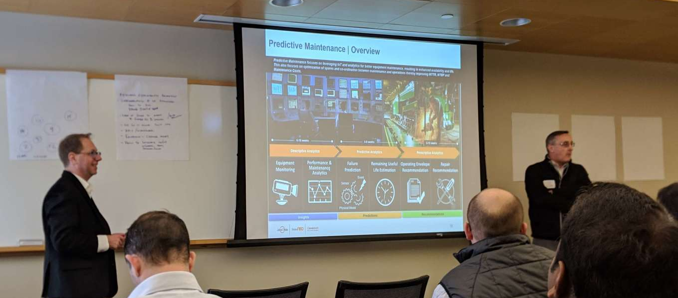 Two men giving a presentation. On the screen is a slide about predictive maintenance.