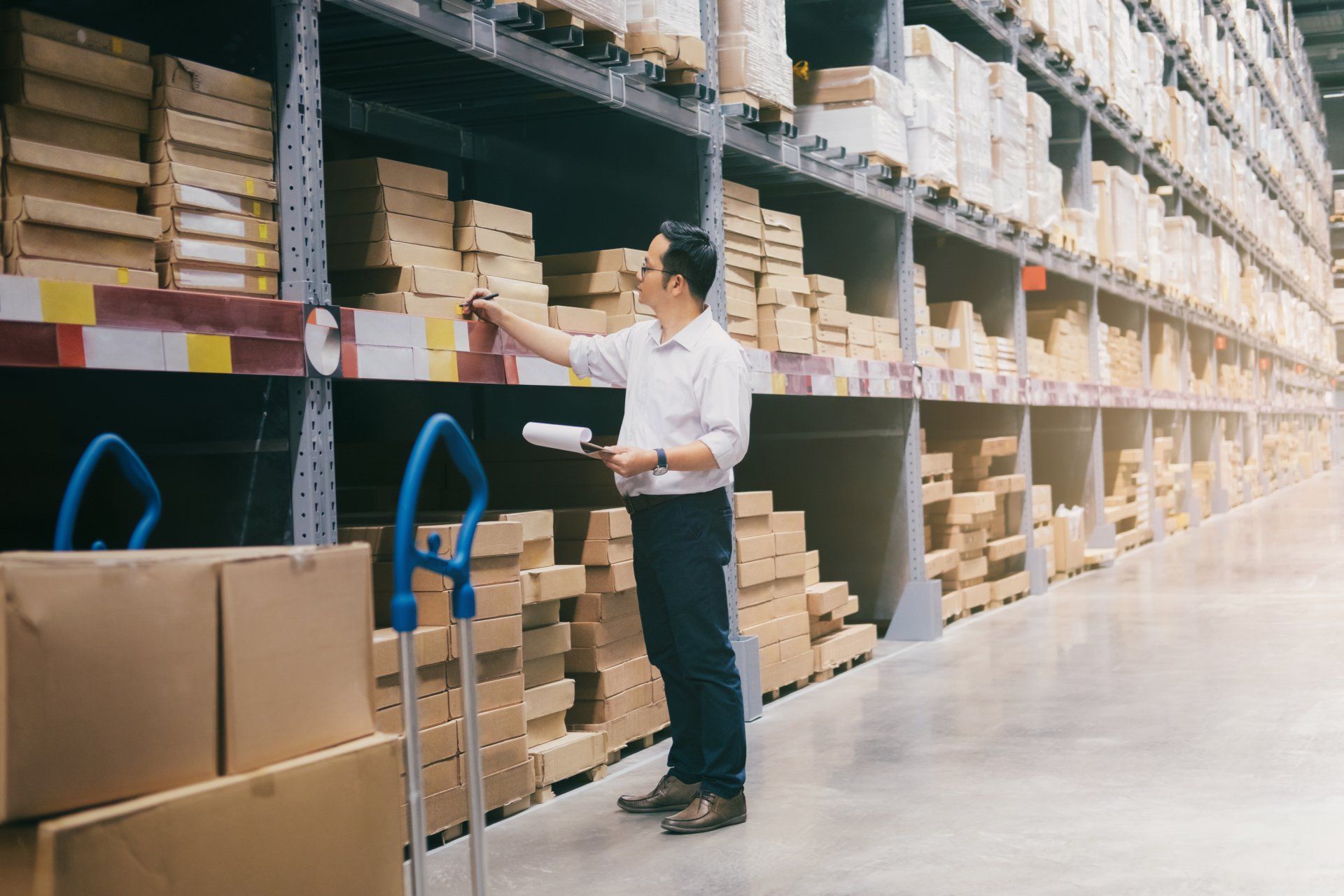 A man taking inventory in a warehouse with many boxes.