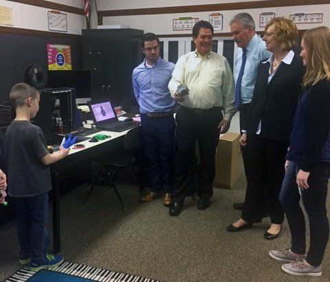 Seifert employees next to a table with various items over top of it. A child is holding and inspecting a 3D printed hand.
