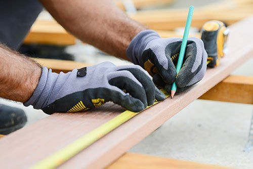 Close up detail of manual worker hands working with a measuring tape and pencil in wood plank