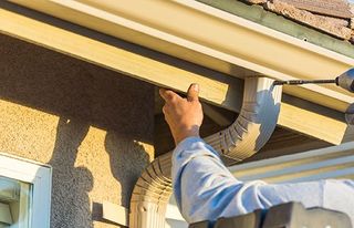 Worker Attaching Aluminum Rain Gutter to Fascia of House