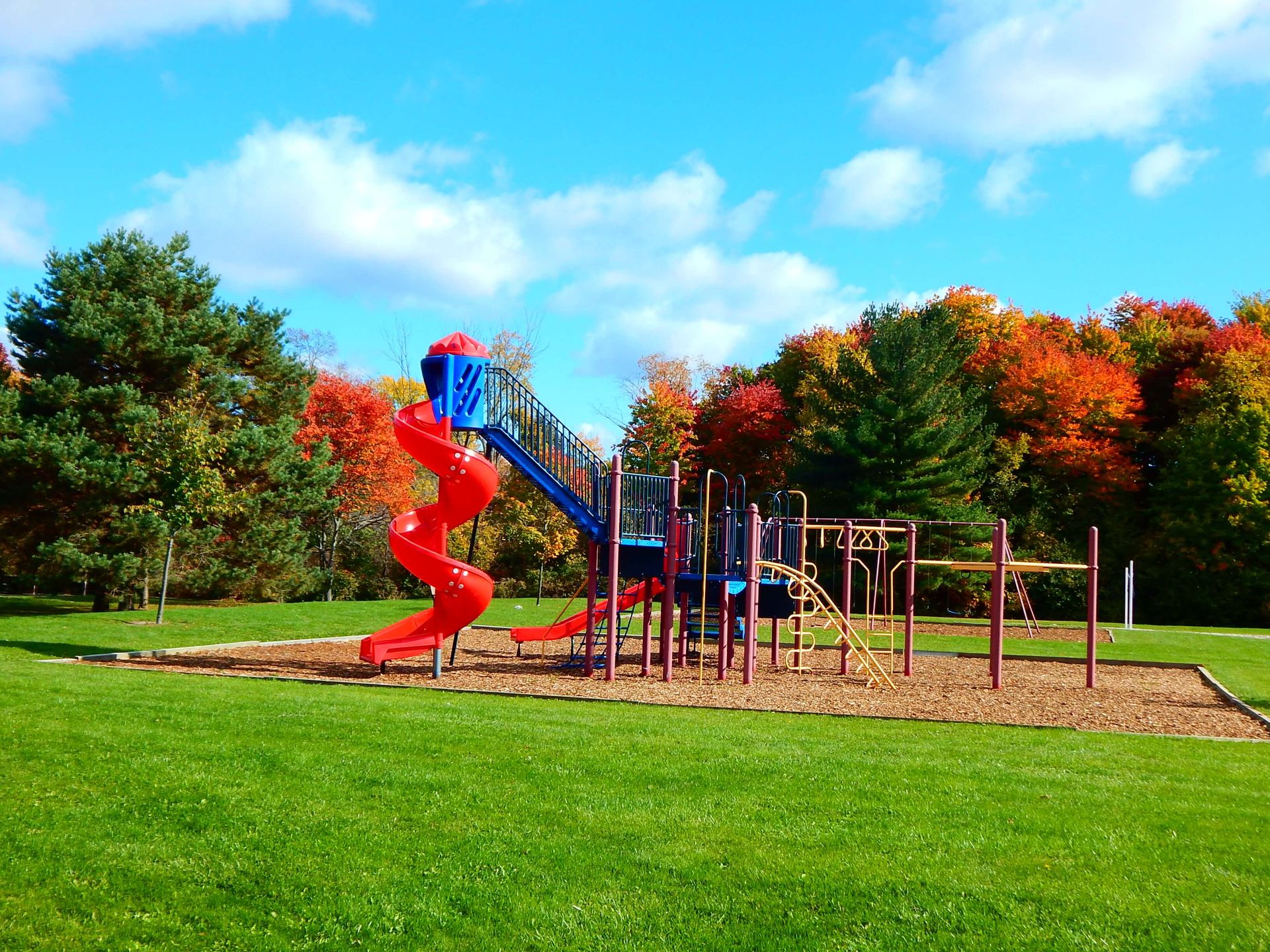 A playground with a red slide and a blue slide in a park.