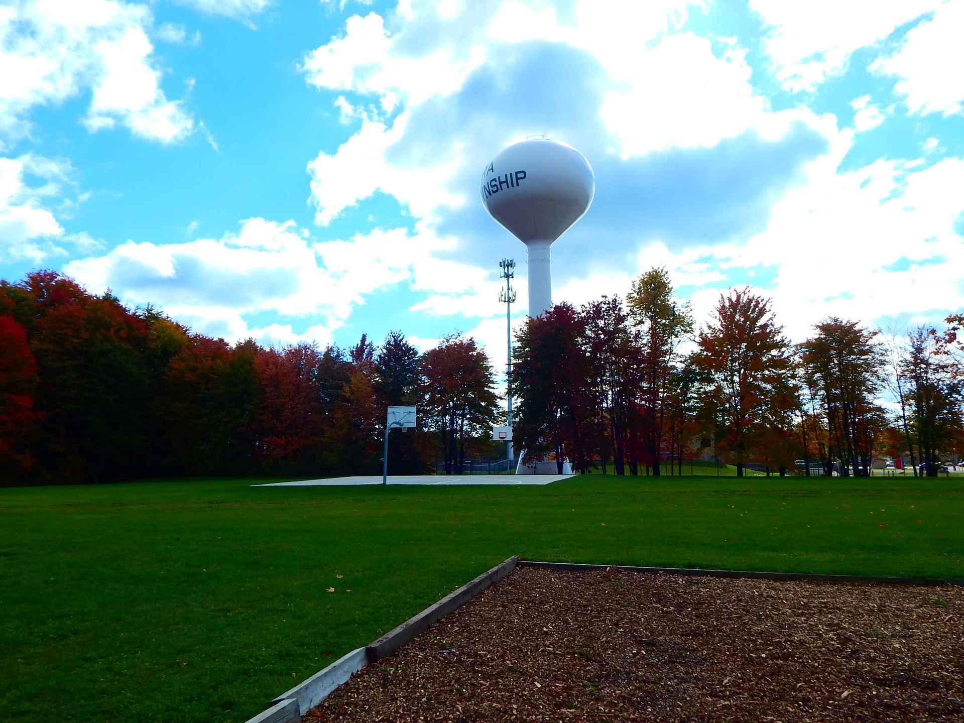 A water tower in a park with a basketball court in the background.