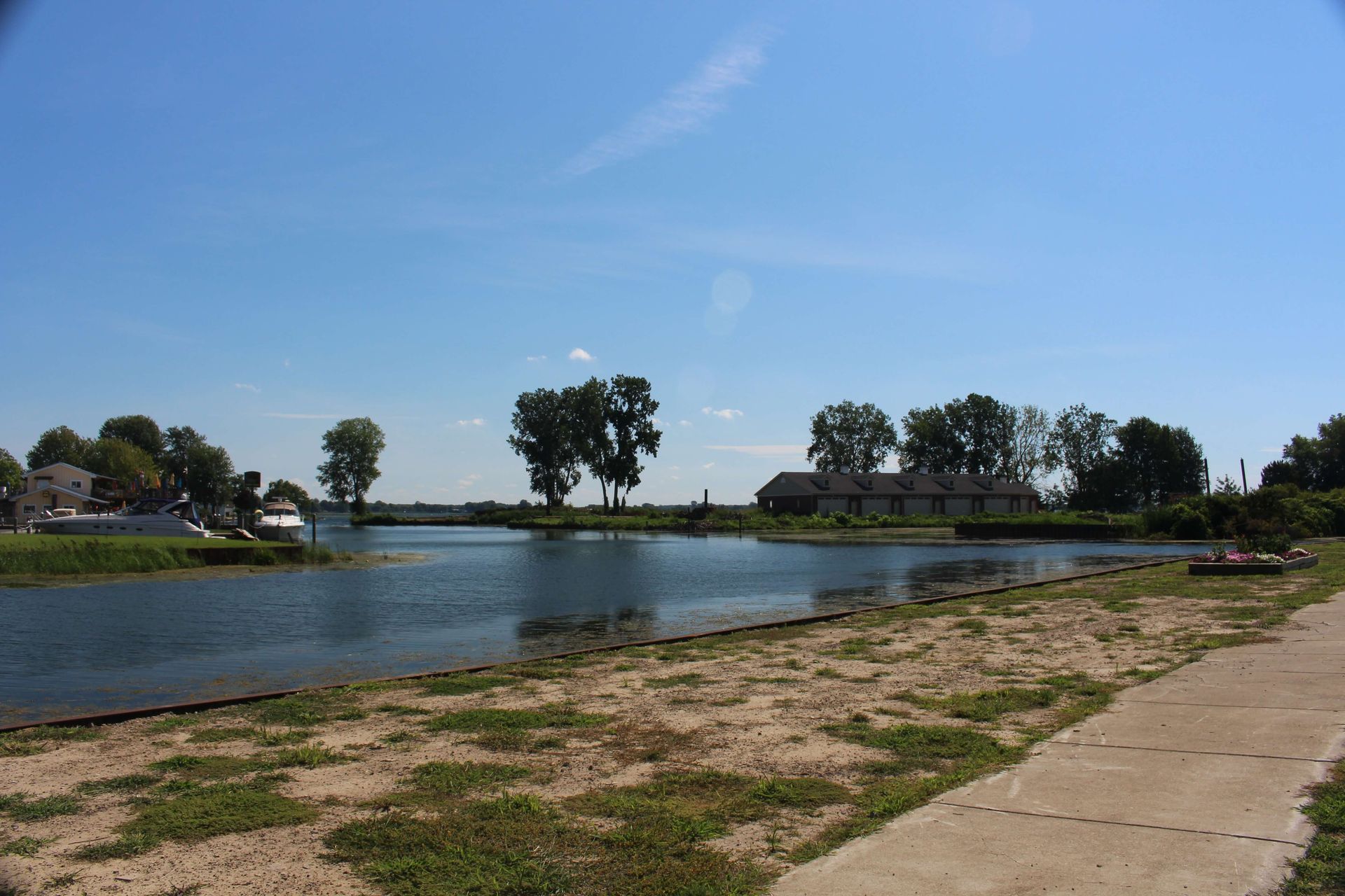 A concrete path leading to a body of water with trees in the background.