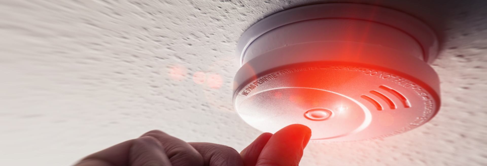 A person is pressing a button on a fire alarm.