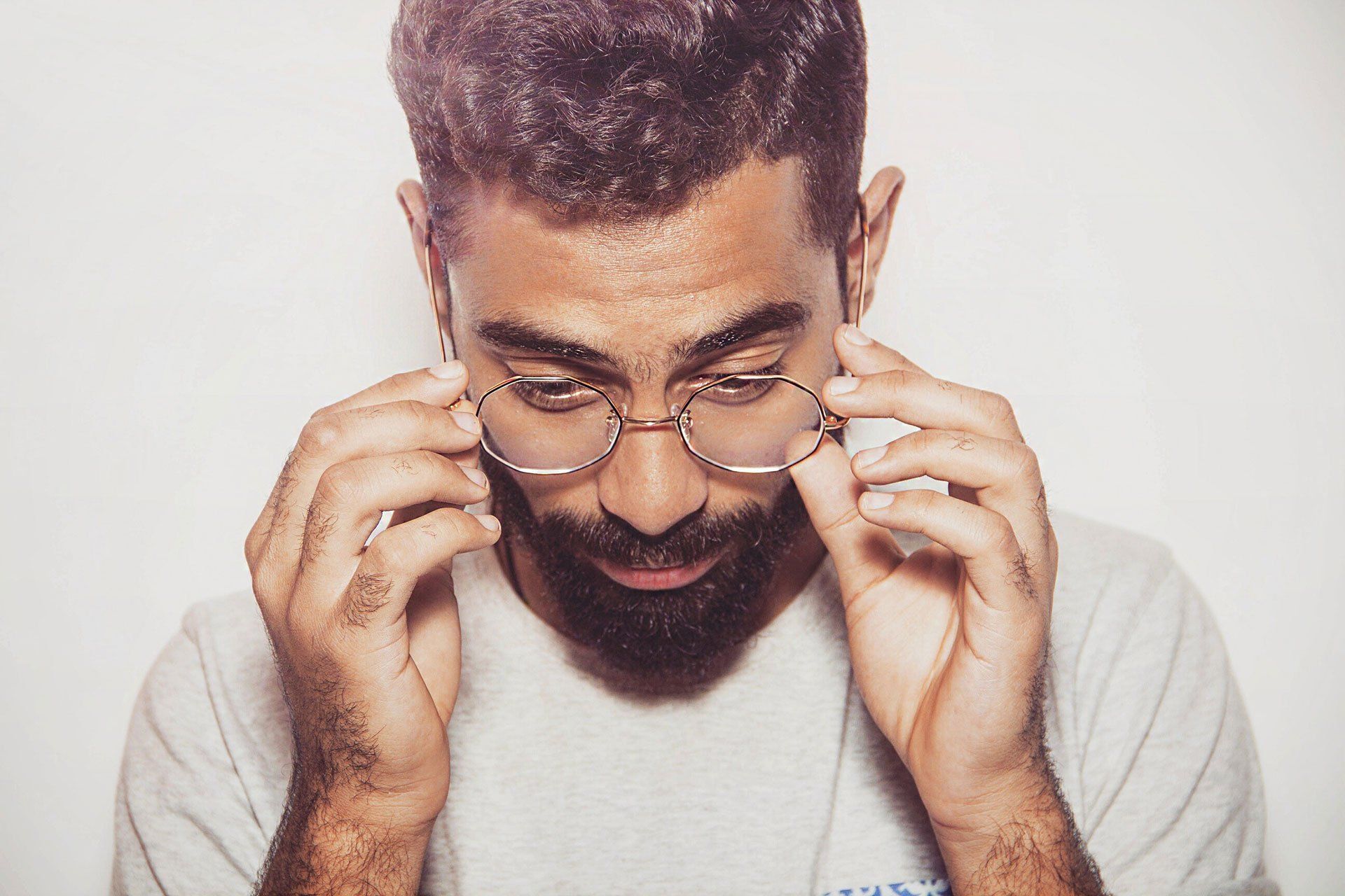 A man with a beard is adjusting his glasses.