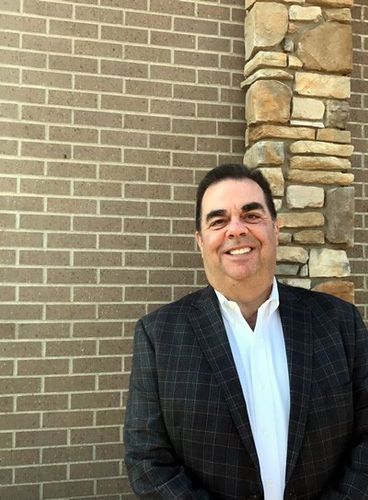 A man in a suit is smiling in front of a brick wall