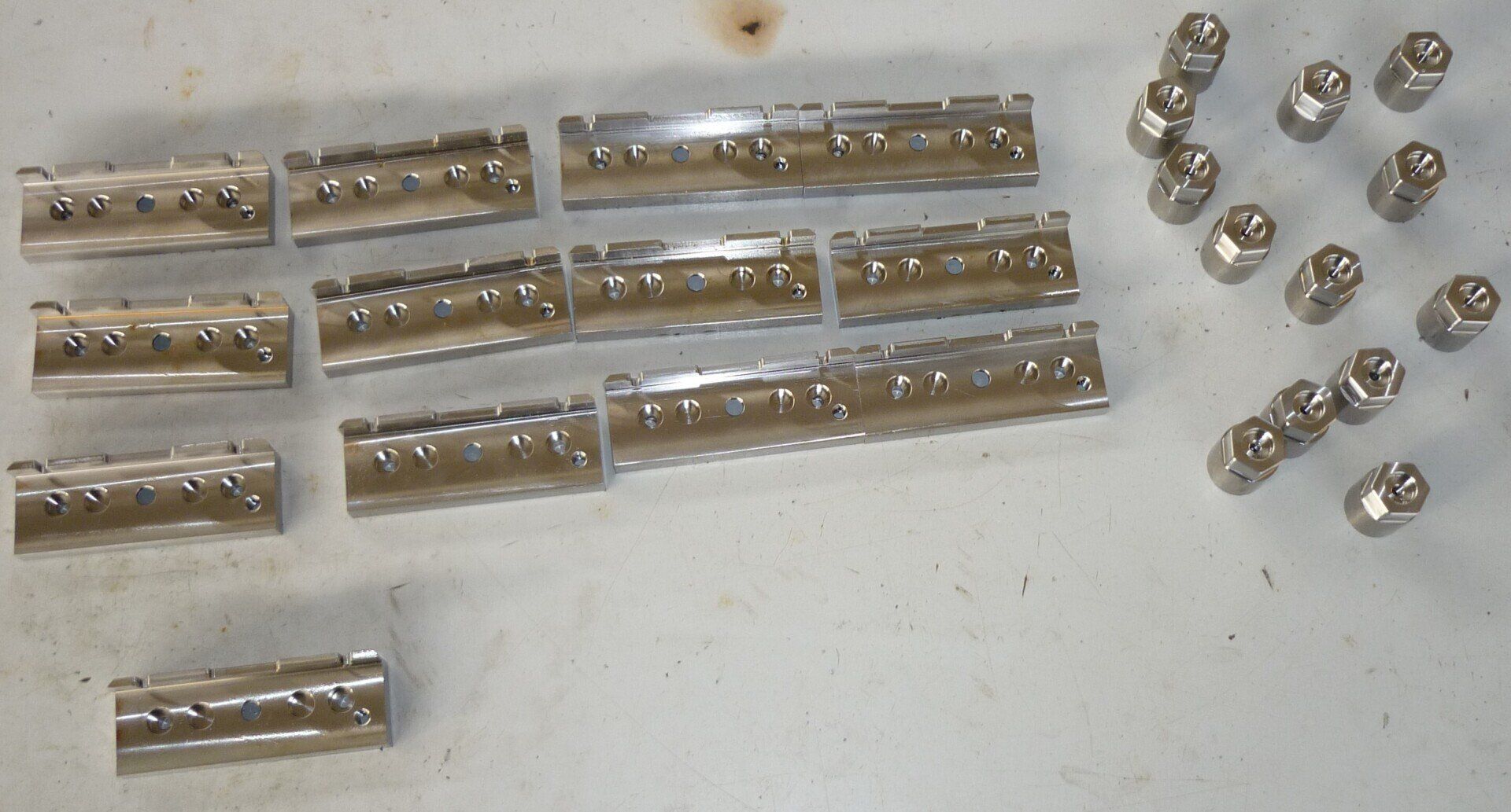 Componenti metallici: file di barre rettangolari con viti e numerosi dadi esagonali, su una superficie leggera.