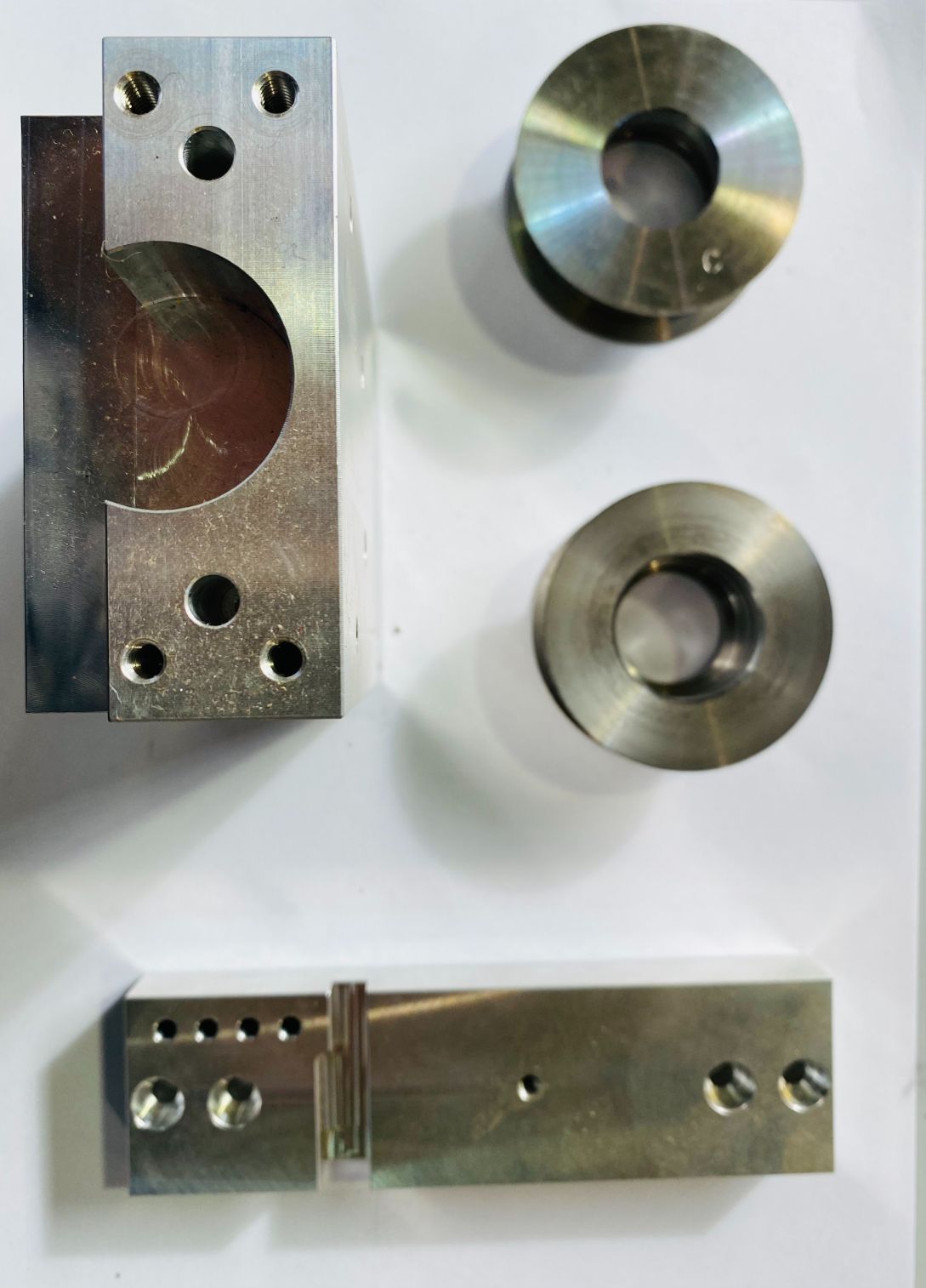 Parti metalliche lavorate, tra cui un blocco con una rientranza circolare, una sezione rettangolare e due dischi circolari.