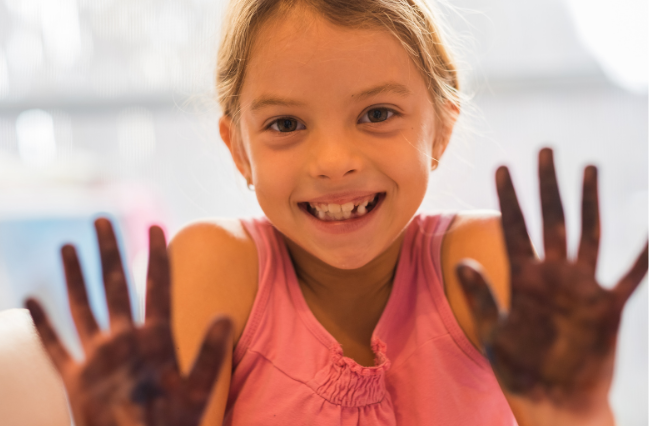 Smiling child with paint-covered hands pressed toward the camera