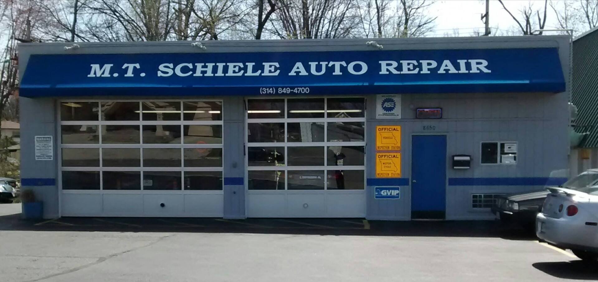M.T. Schele Auto Repair storefront with blue awning and garage doors, parked car at right