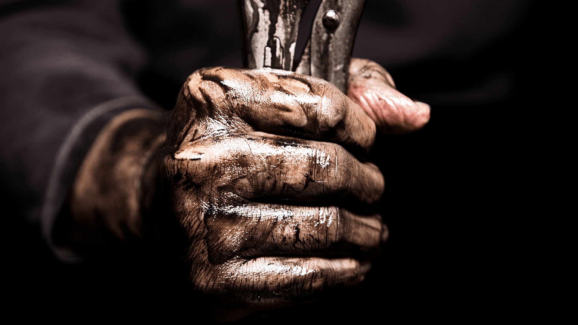 Dirty hands clasping a vertical wooden stick against a dark background