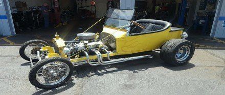 Yellow vintage hot rod with exposed chrome engine parked outdoors