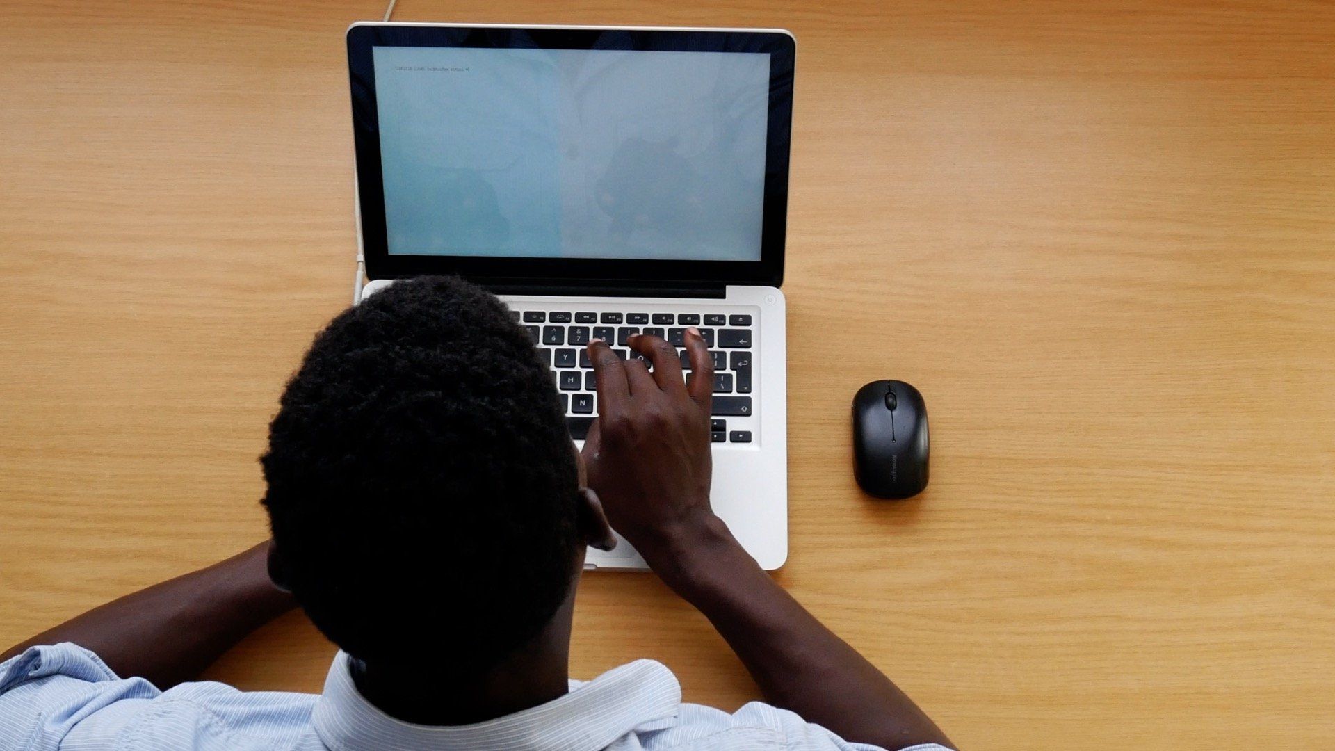 A man is typing on a laptop computer on a wooden desk.