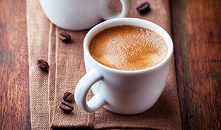 A cup of coffee is sitting on a wooden table next to coffee beans.