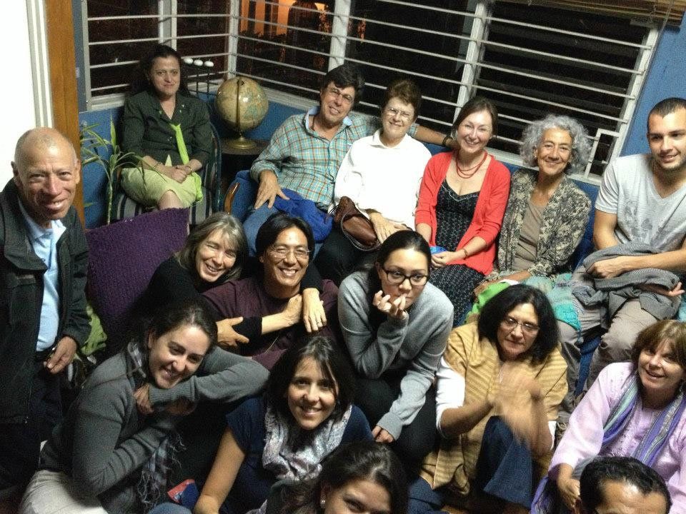 Group of people indoors, smiling and posing for a photo. Some seated on a blue couch, others in front.