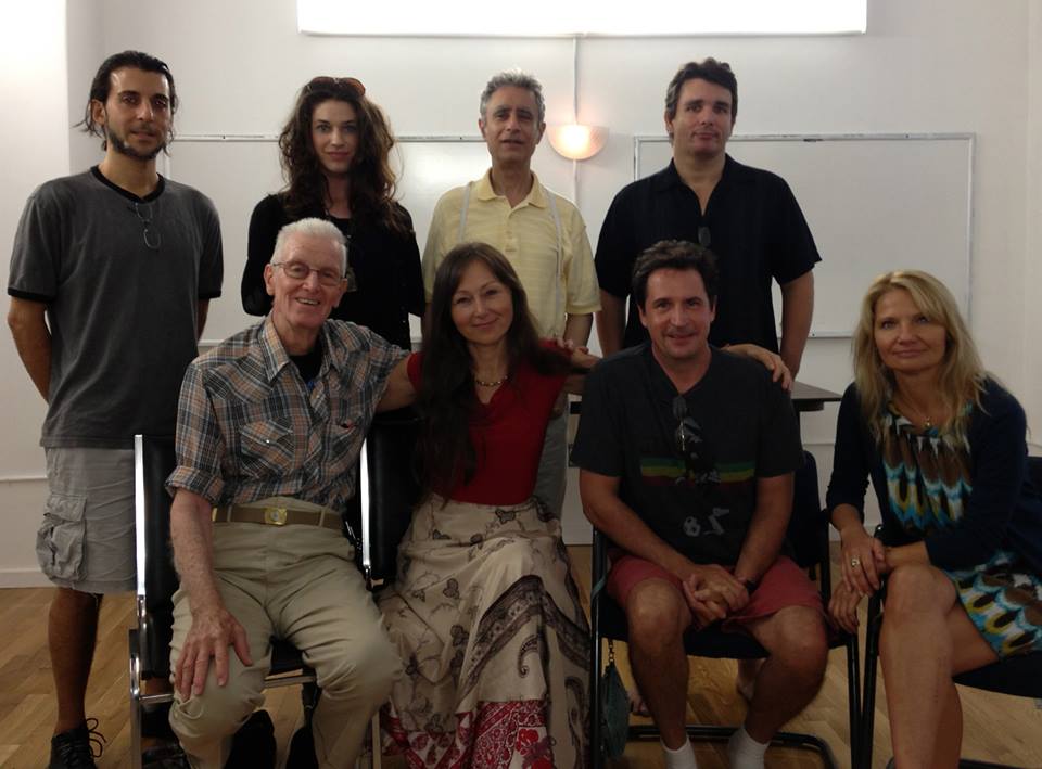 Group of people posing for a photo indoors, some seated. They are smiling, with a white board in the background.