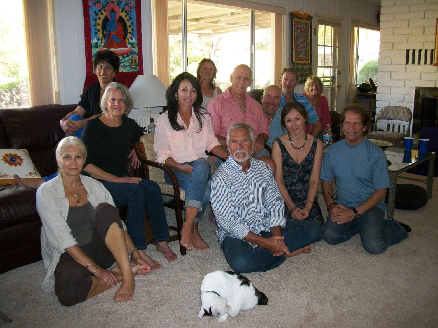 Group of people sitting on floor and couch in a living room, with a cat.
