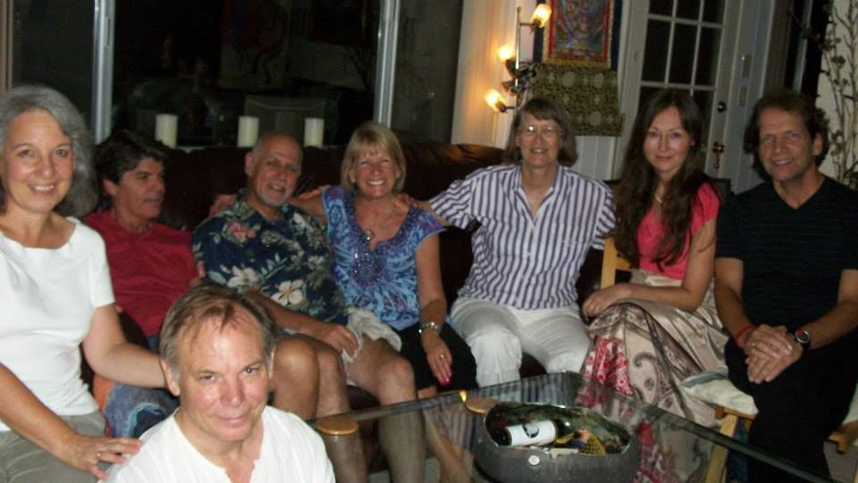 Group of people smiling on a sofa, inside a warmly lit room with a coffee table in front.