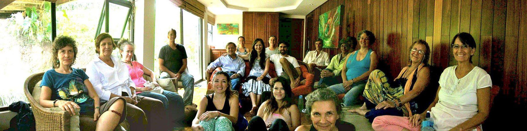 Group of people seated indoors, near windows and wooden paneling. Some smile, some are looking at the camera.