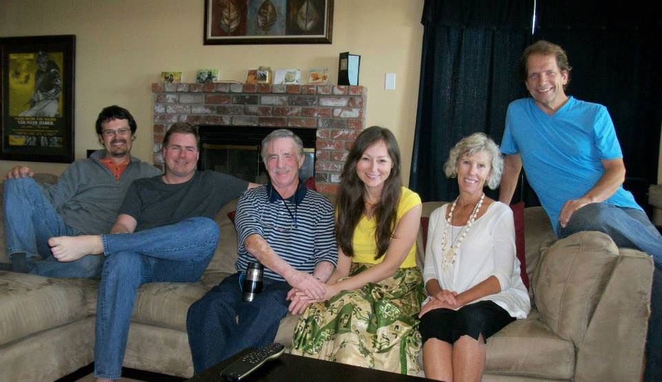 Family seated on a sofa indoors. People smiling, posing for a photo, brick fireplace visible.
