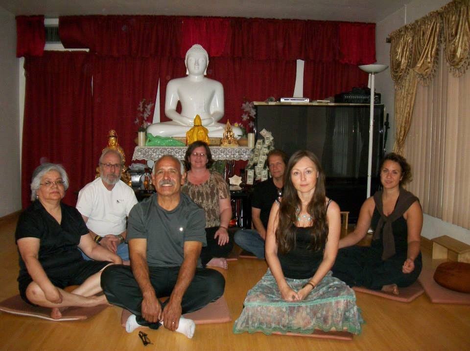 Group seated in front of a Buddha statue in a room, meditating.