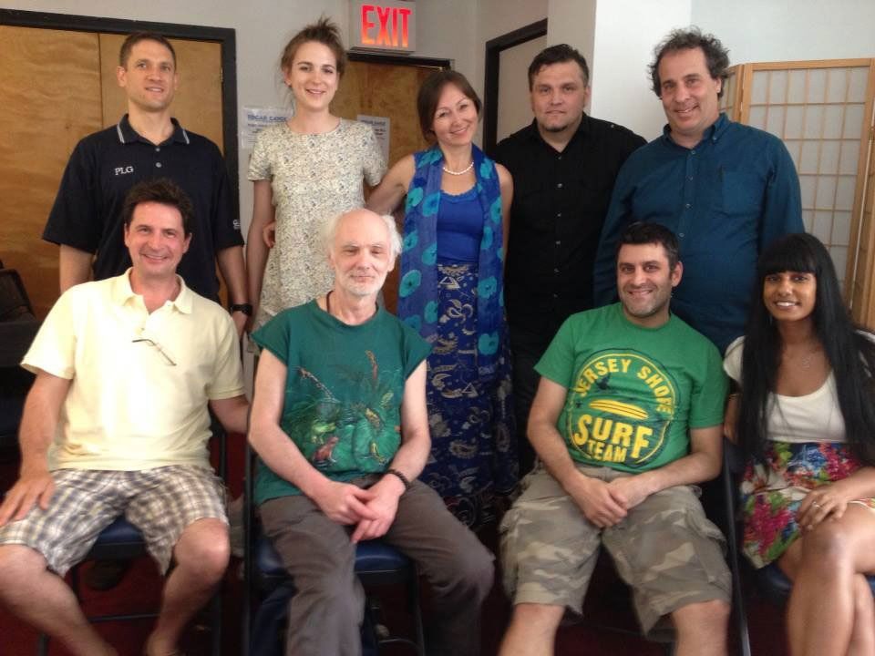 Group of people posing for a photo indoors. Some seated, some standing. One woman in blue, others wearing various casual clothing.