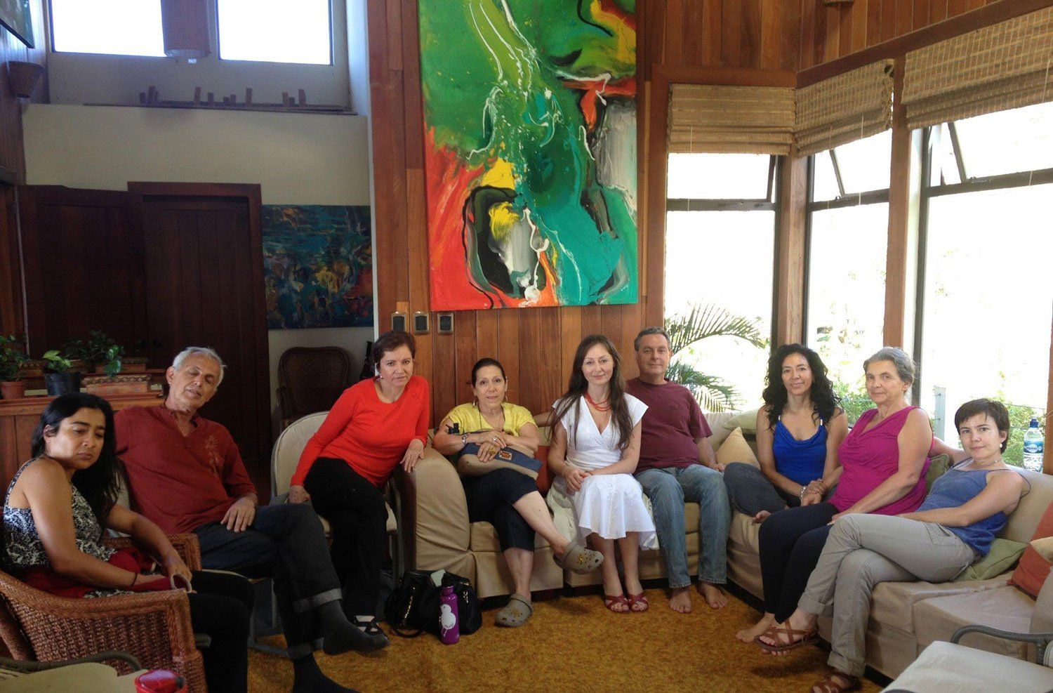 Group of people seated in a living room with an abstract painting. Some are looking at the camera.
