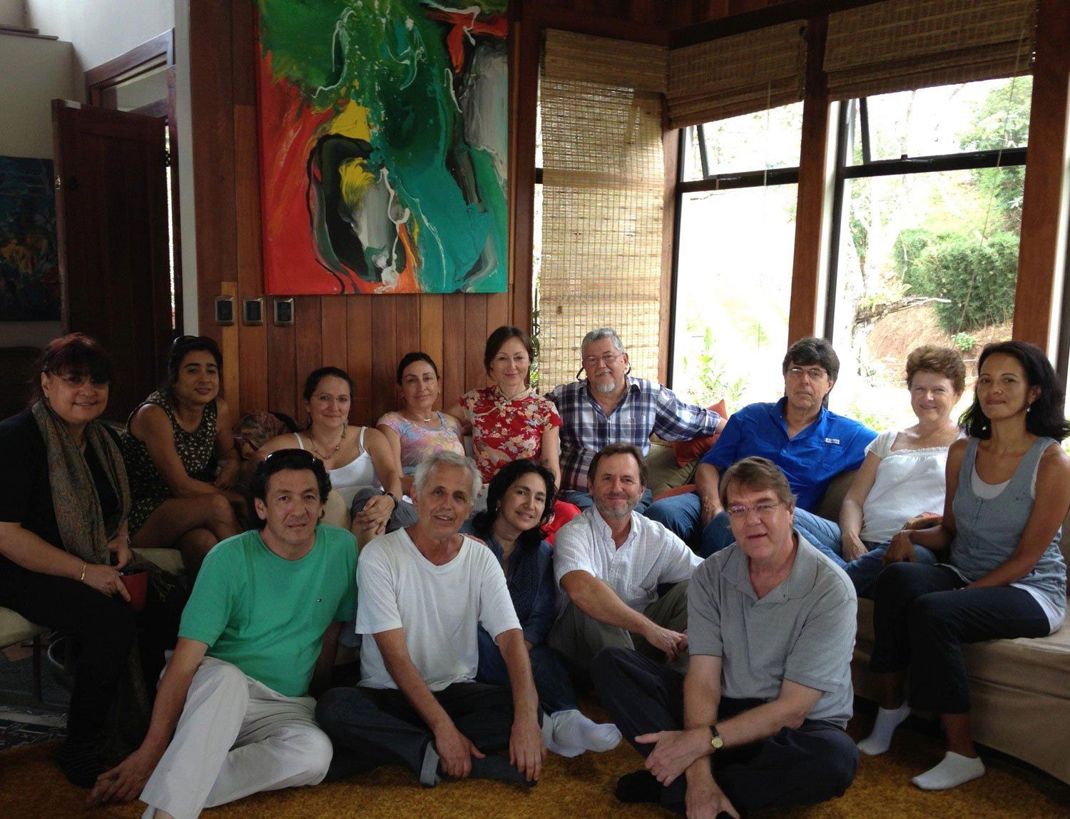Group of people sitting and standing indoors near a window. A colorful painting hangs on the wall.