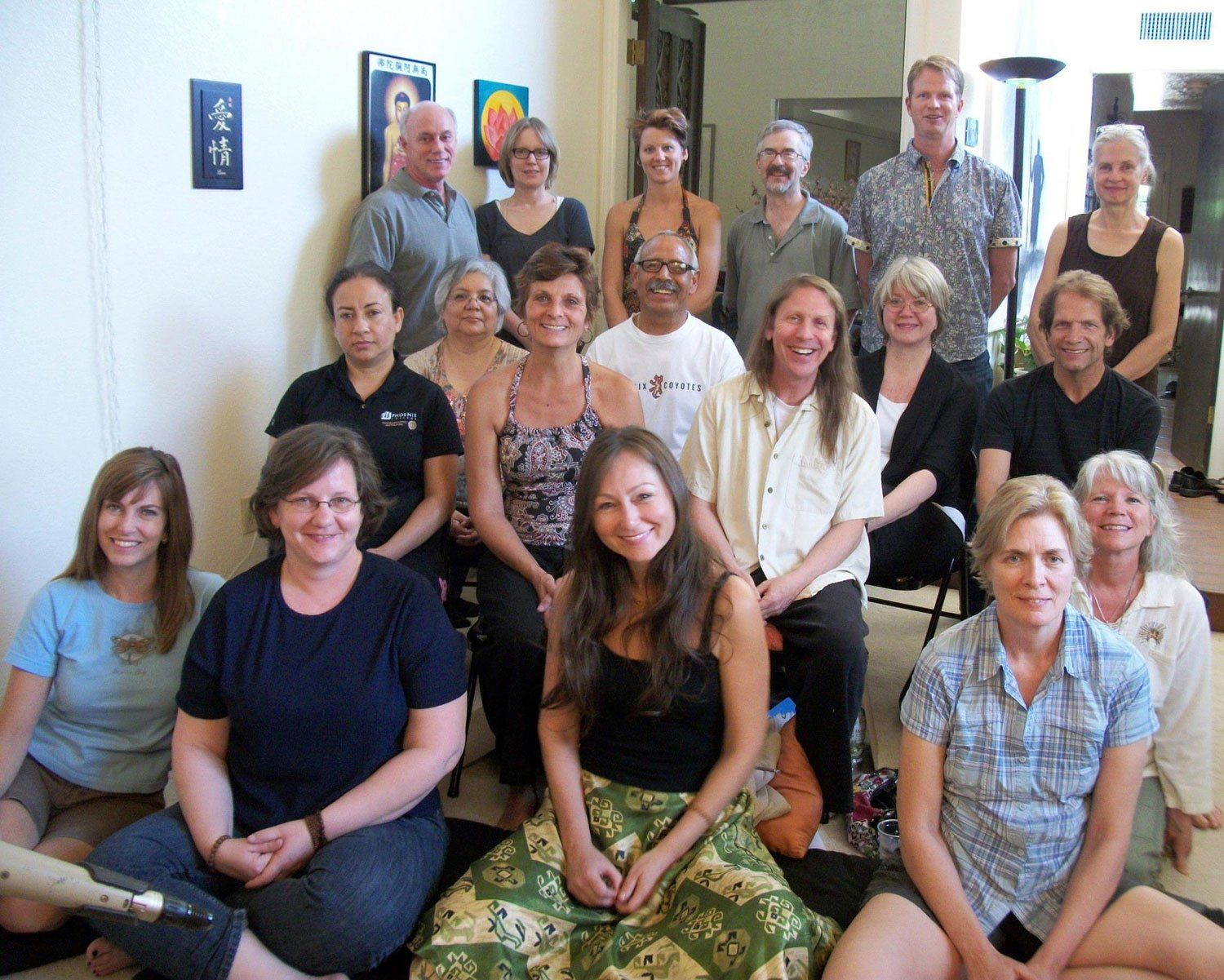 Group of people posing together indoors, smiling. Some sitting, others standing. Well lit room.