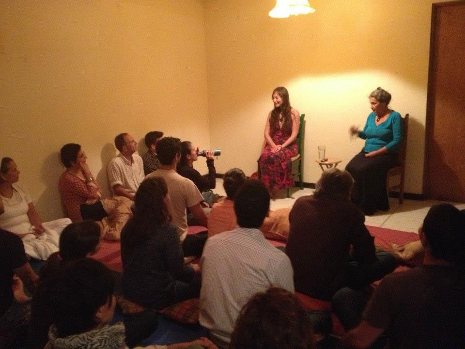 People seated on floor listening to two women speaking in a room.
