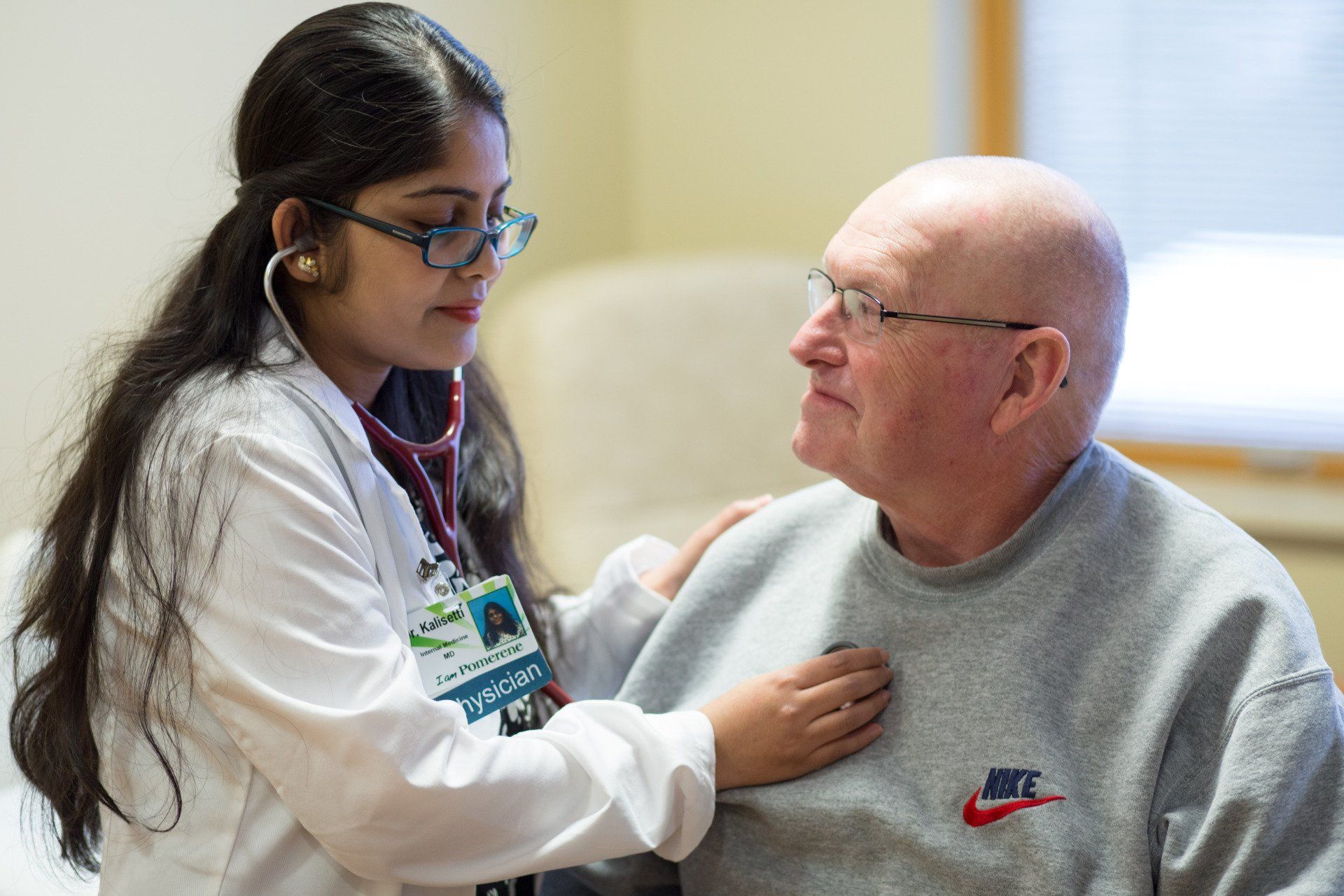 Doctor listening to elderly patient's chest with a stethoscope; indoor setting.
