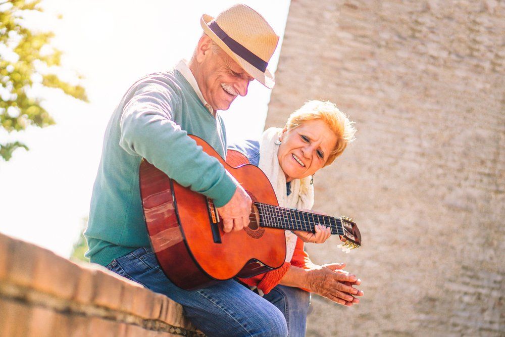 Older person playing guitar for another outdoors.