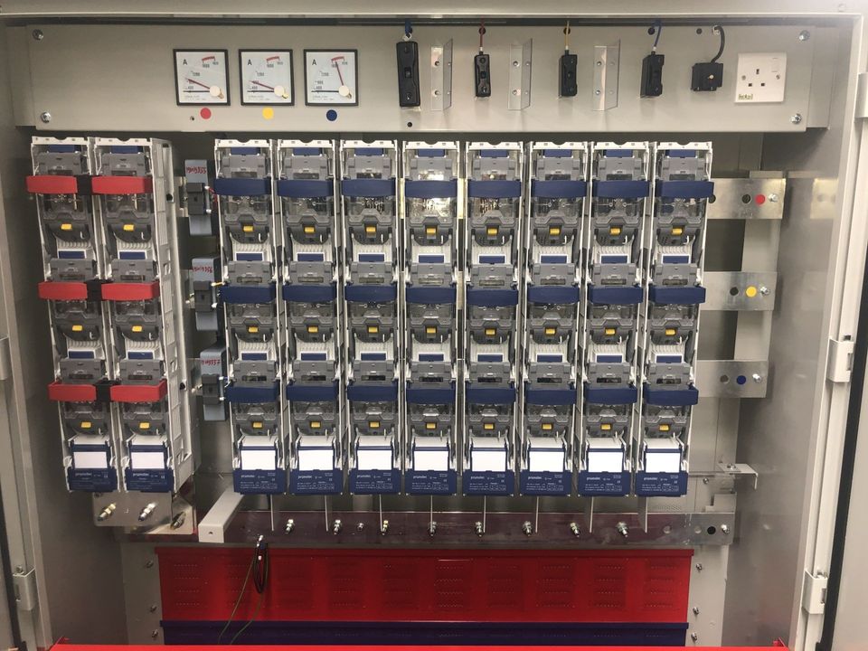 Electrical panel with rows of circuit breakers, wiring, meters, and red and blue accents.
