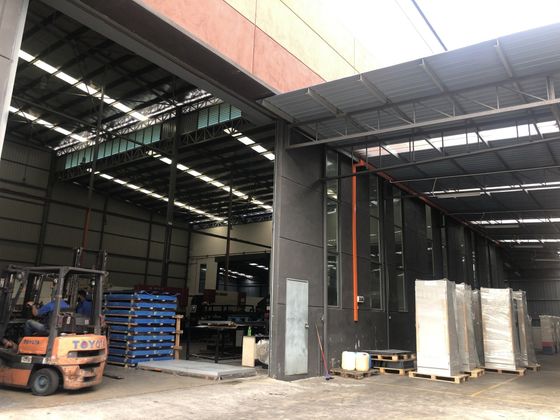 Forklift loading pallets at an industrial warehouse entrance; gray walls, metal roof, sunlight.