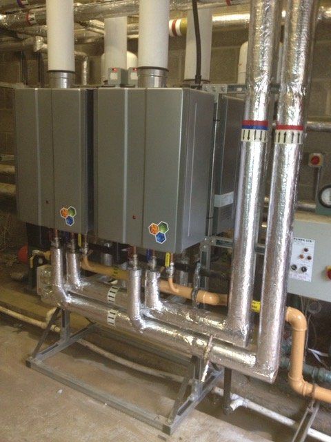 a row of boilers are lined up in a room with pipes .