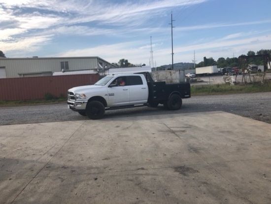 A white truck with a flat bed is parked in a parking lot